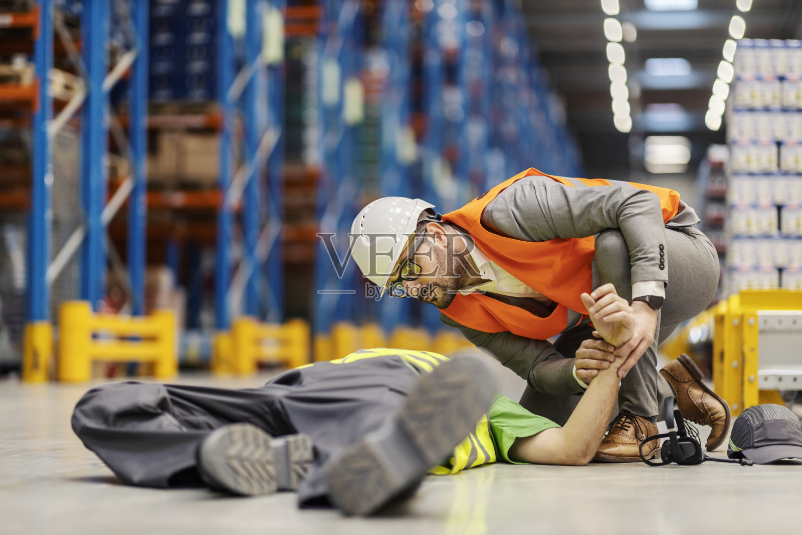 一个仓库工人躺在地上不省人事,他的主管正在给他急救。照片摄影图片