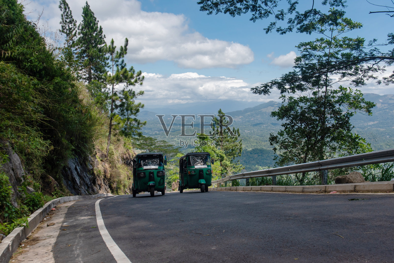 在一个阳光明媚的日子里,两辆卡车行驶在斯里兰卡蜿蜒的道路上,周围环绕着绿色植物。照片摄影图片