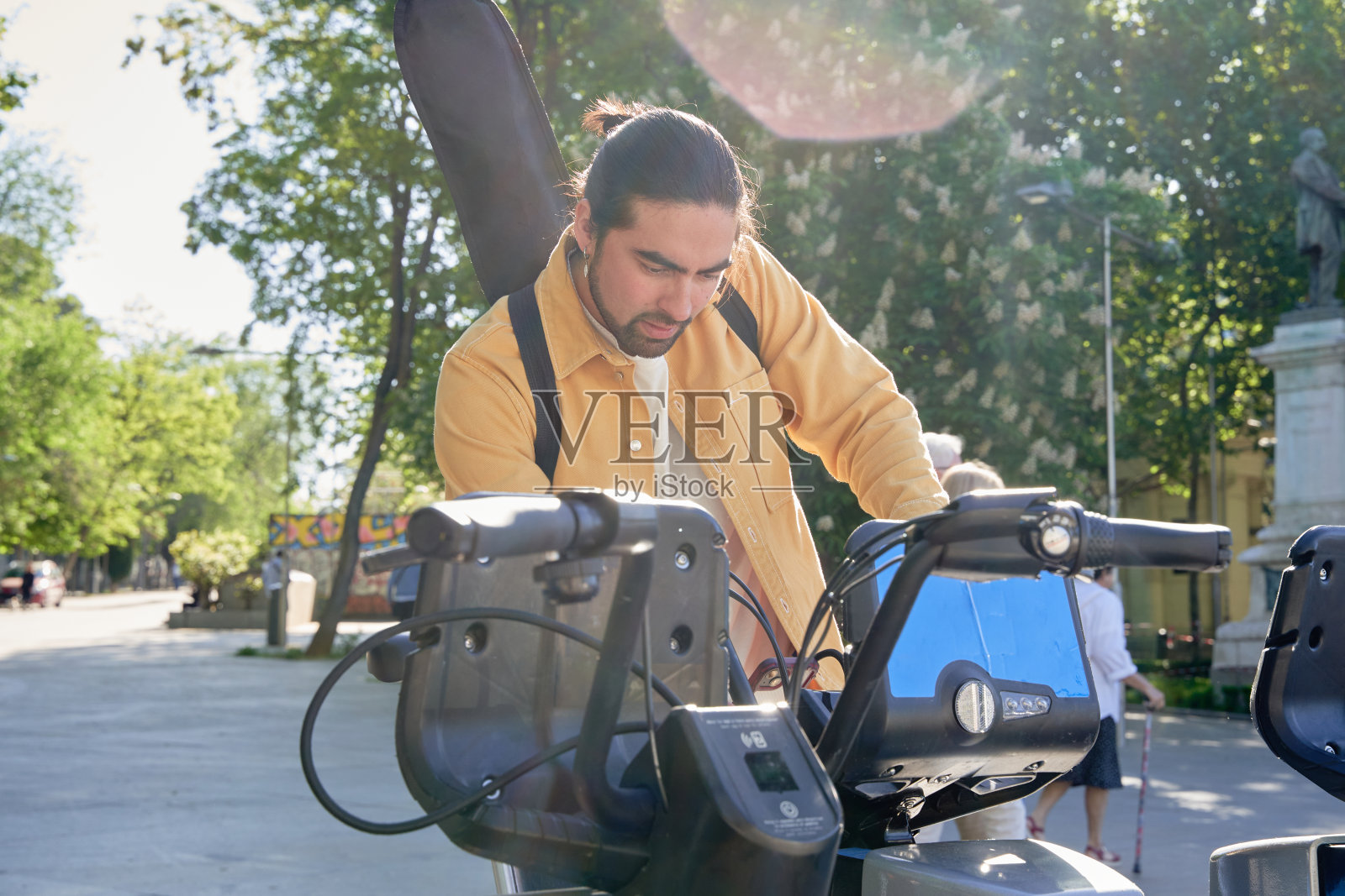 一个穿黄色夹克的男人看着一辆蓝白相间的自行车。自行车可以停在路边出租,在城市里四处行驶也不会造成污染。照片摄影图片