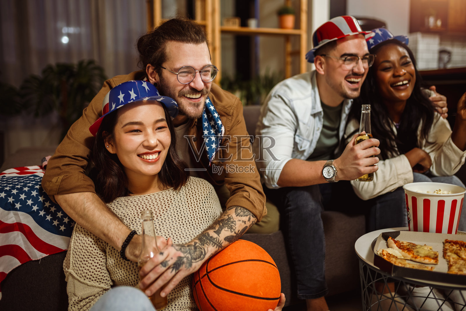 一群来自不同种族的朋友,在美国国旗下观看篮球比赛,喝着啤酒欢呼。照片摄影图片