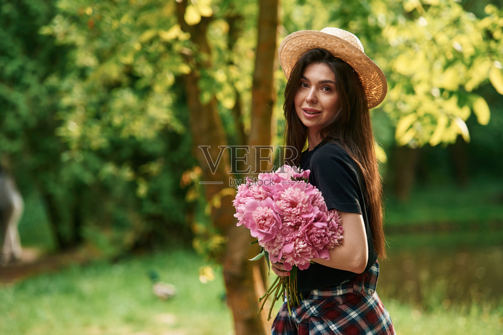 戴着草帽。美丽的年轻女子在公园里捧着牡丹照片摄影图片