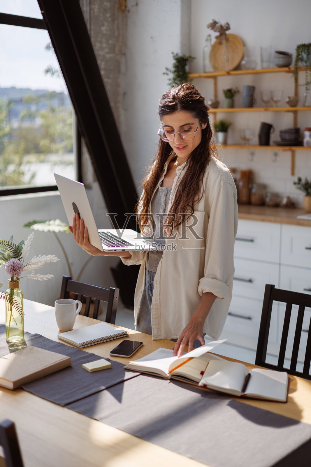 早上戴眼镜的女人拿着笔记本电脑在厨房看书照片摄影图片