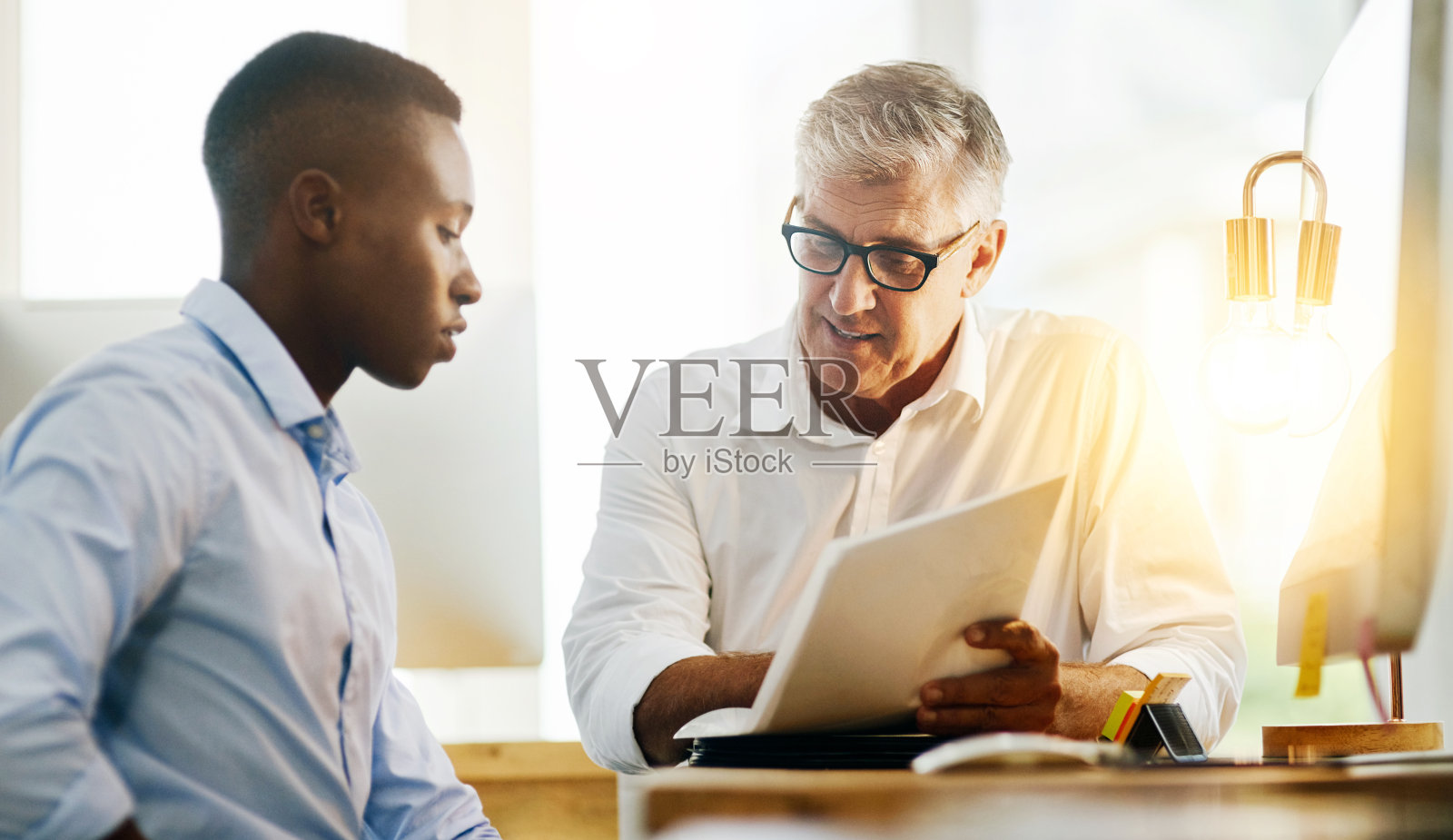 男性老板,文书工作和员工在办公室指导,审查和讨论在办公桌上。成熟的领导者,在工作场所通过文件,合同和辅助阅读进行招聘和解释照片摄影图片