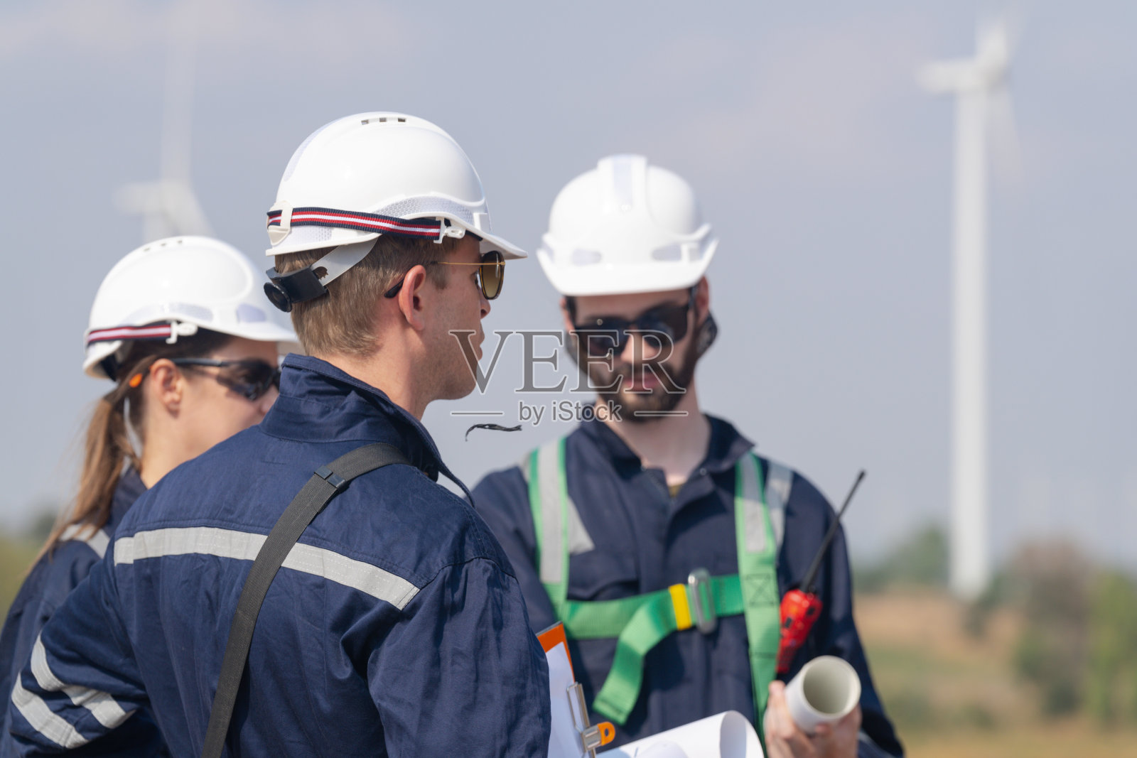 工程师男和女检查风力涡轮机农场的建设。由超级能源公司运营的带有储能系统的风力涡轮机。工人们开会检查周围的区域。照片摄影图片
