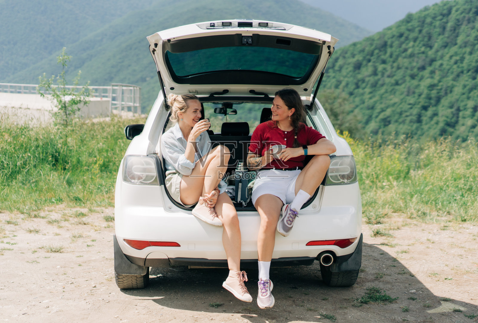 两个女性朋友在出城旅行时,坐在汽车后座,边聊天边喝着保温瓶里的咖啡。照片摄影图片