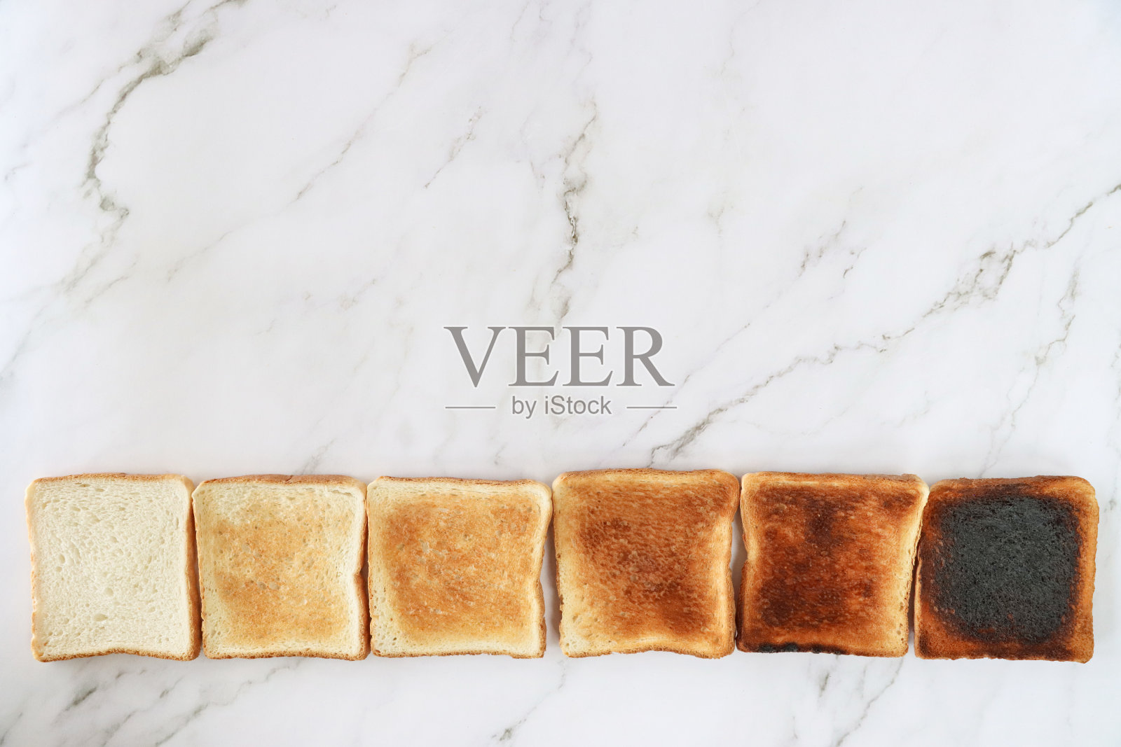 渐变颜色的六片烤面包的特写图像,一排烤白面包,未熟到烧焦的颜色范围,白色大理石效果背景,抬高视野,复制空间照片摄影图片