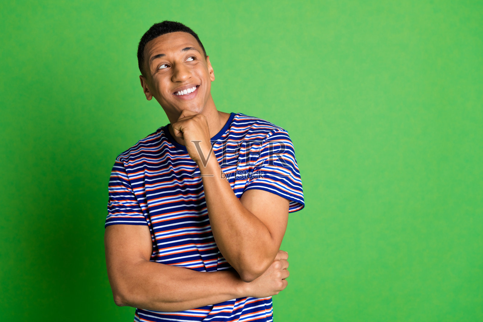 照片中聪明伶俐的男人穿着条纹时髦的衣服,摸着脸,在绿色的背景上显得空无一物照片摄影图片