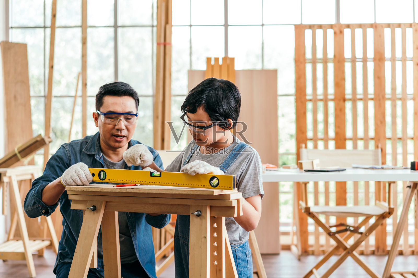 特写:木工手戴着工作手套,用铅笔在木板上画出切割线。建筑业、木工车间。木匠在做木板。木工的概念。照片摄影图片