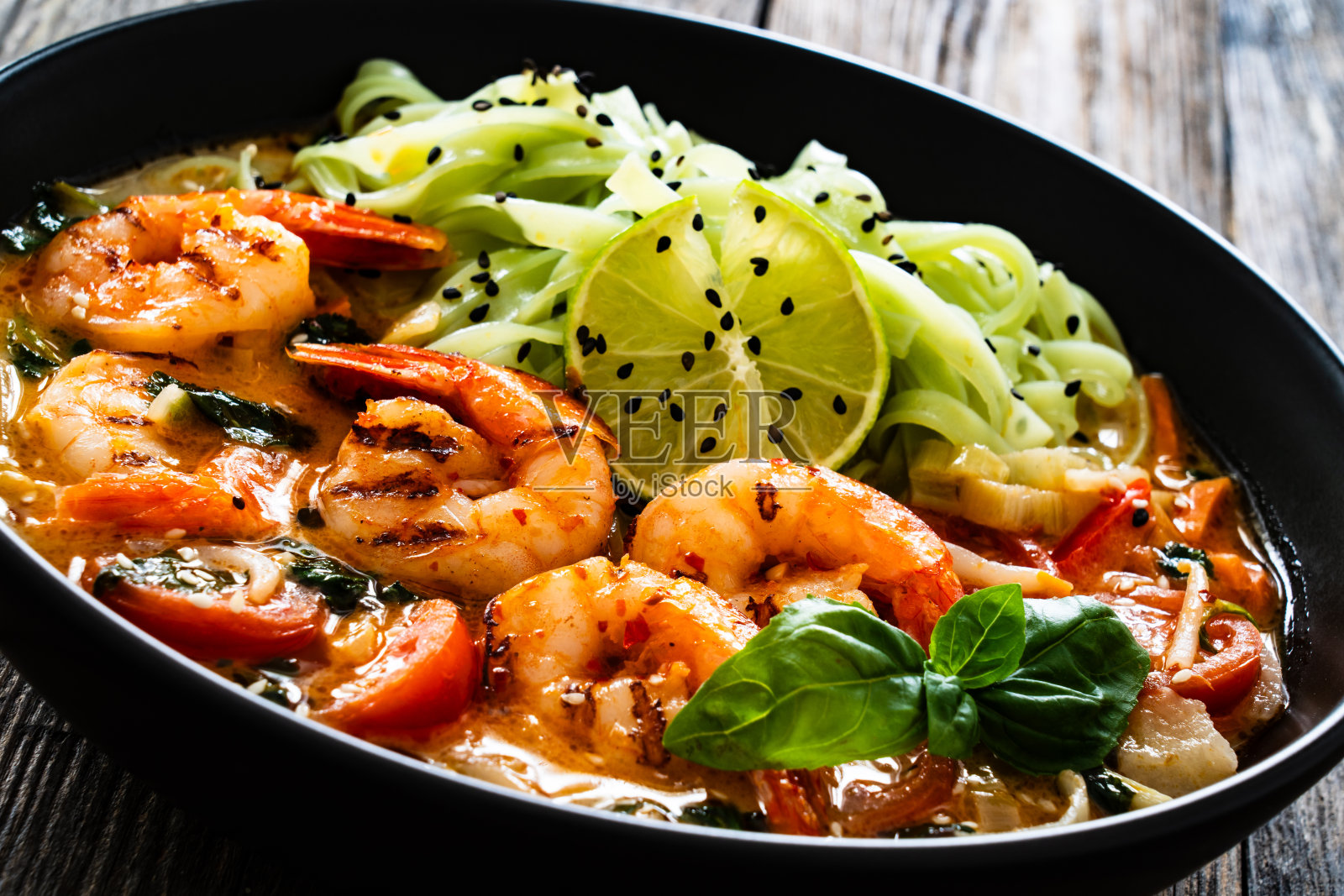 冬阴功汤-泰国汤与虾和米粉在黑碗用筷子在木桌上照片摄影图片