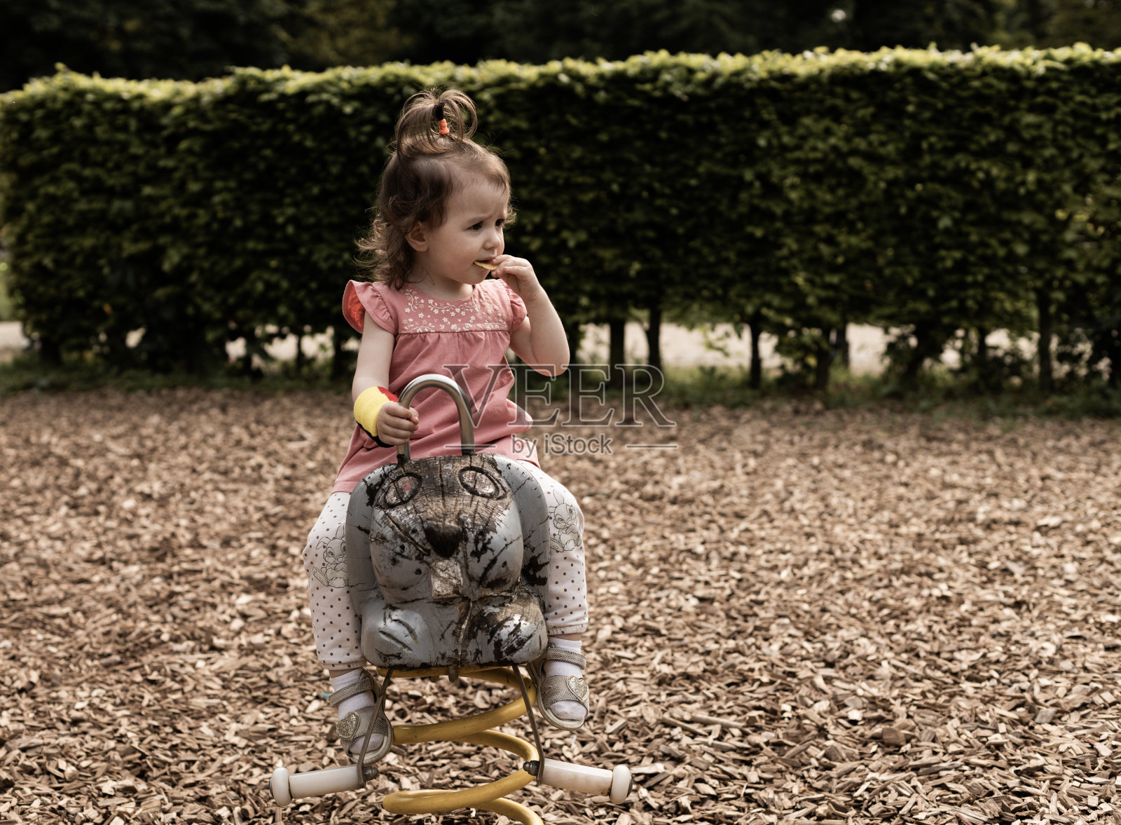 一个快乐的女孩坐在公园里的弹簧木秋千上吃薯片。照片摄影图片