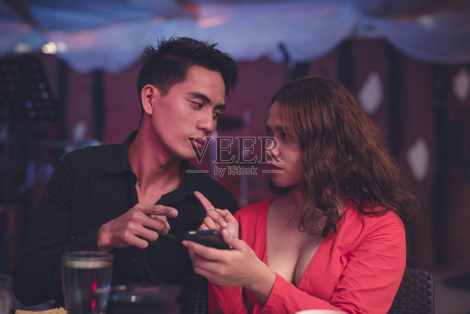 一个男人向他的女朋友解释他手机上另一个女人发来的甜蜜短信。一个女人拿着男友的手机,撞见他和另一个女孩聊天。冲突的概念。照片摄影图片