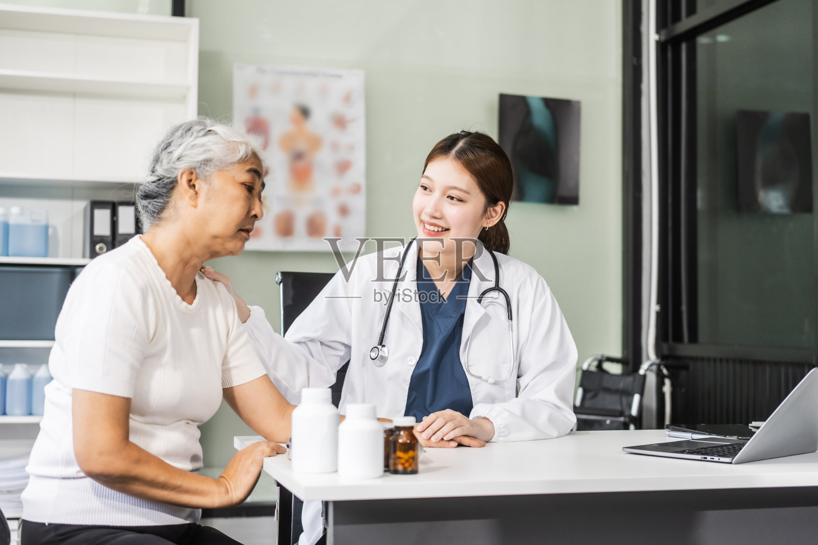 一位年轻的亚洲女护士在她的办公桌上提供医疗服务,照顾一位老年妇女病人。他们在专业的环境中讨论健康清单和医疗建议。照片摄影图片