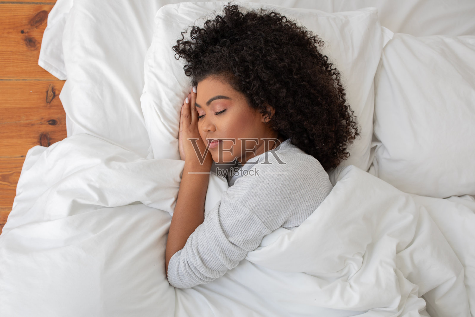 卷毛女人双手抱头躺在床上照片摄影图片