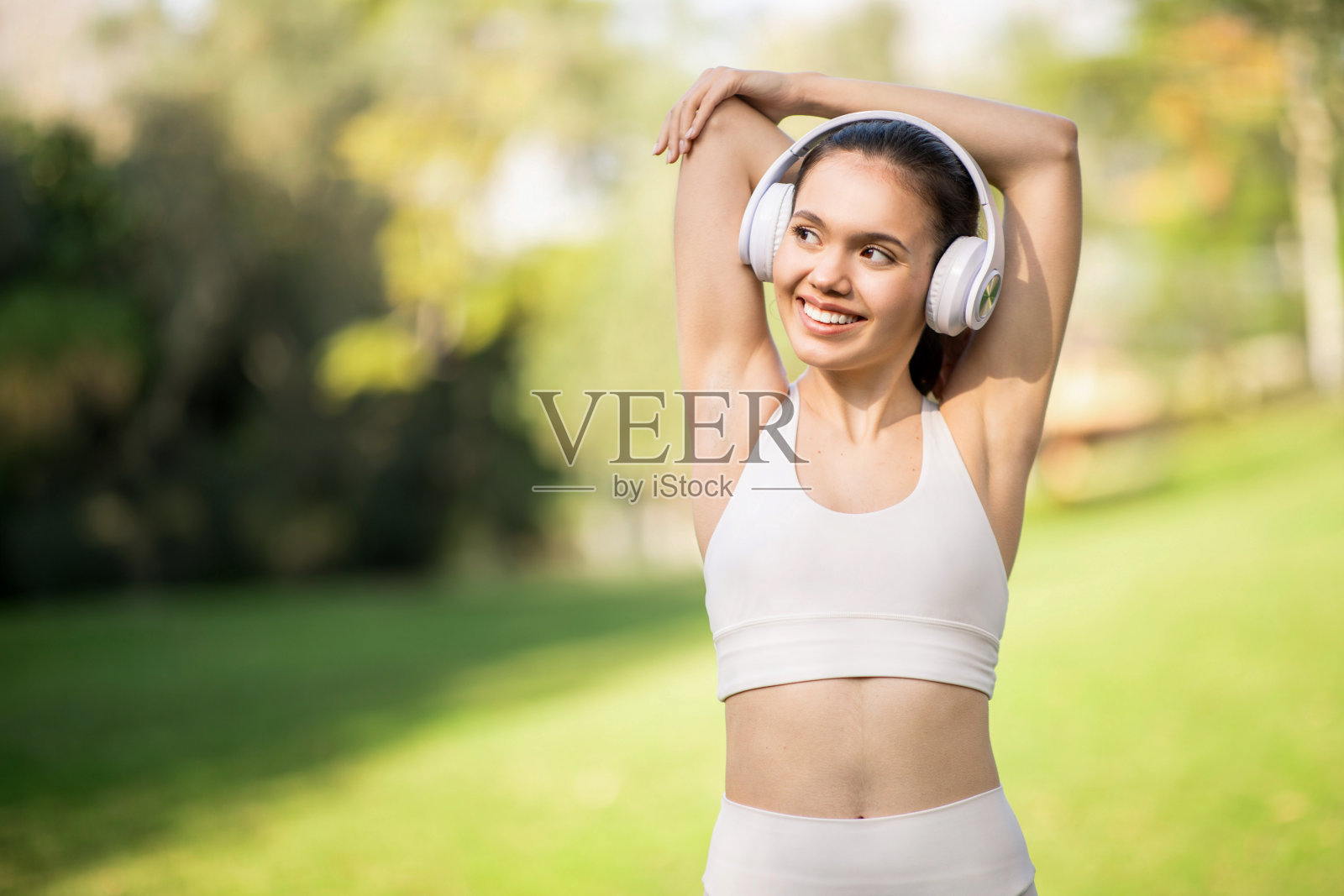一位快乐的年轻女子一边伸伸胳膊,一边戴着白色耳机听音乐照片摄影图片