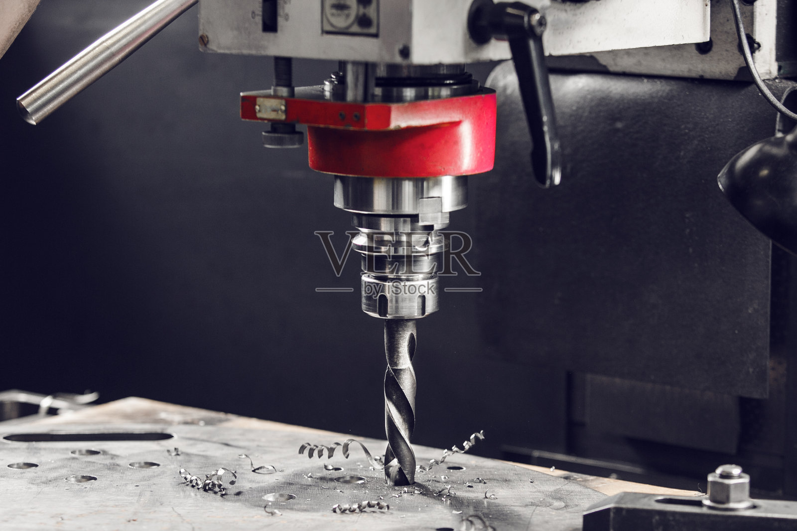 立钻在金属零件上钻孔。金属钻床的特写。照片摄影图片