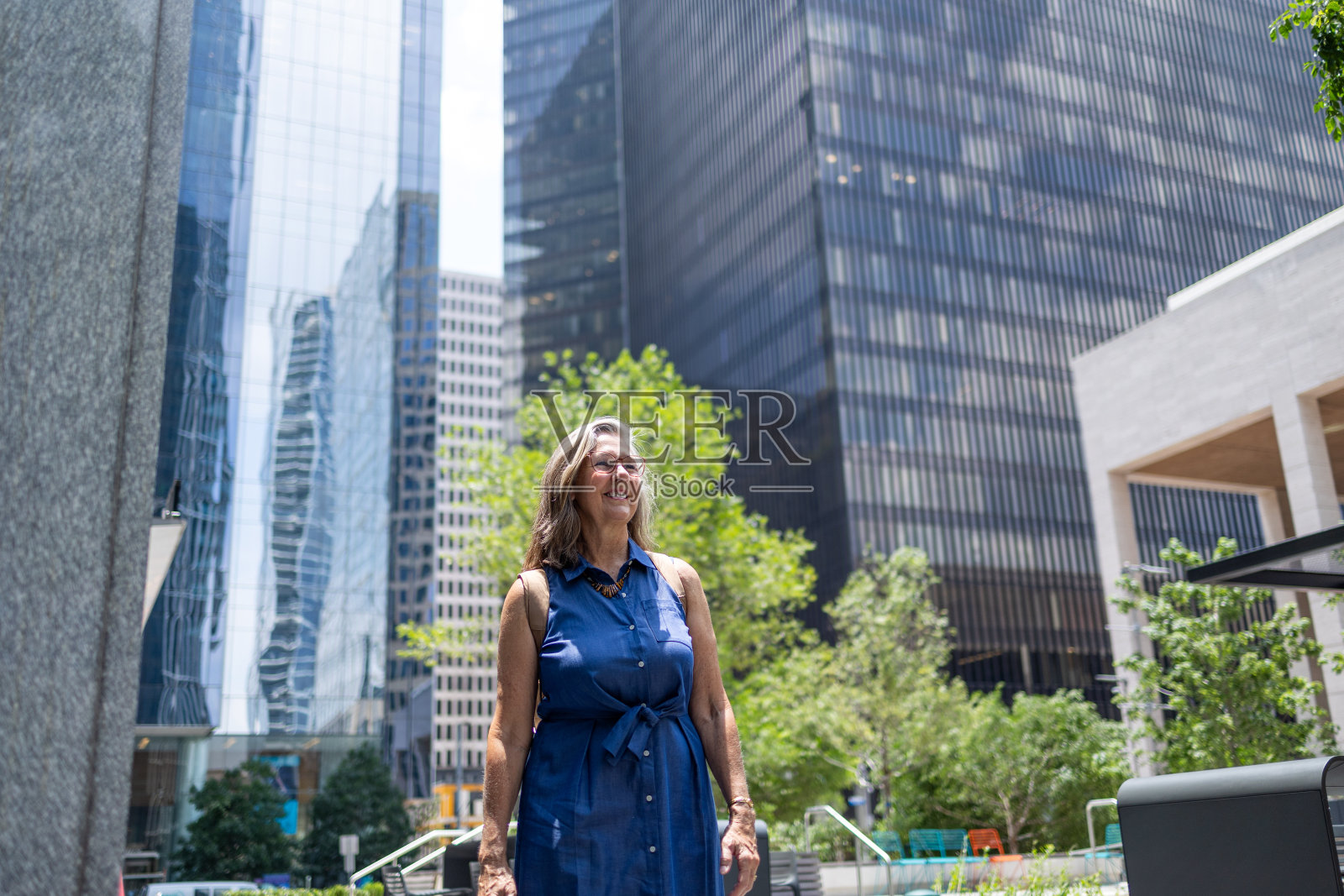 生活在一个有着现代摩天大楼和绿色环境的城市里的老年妇女照片摄影图片