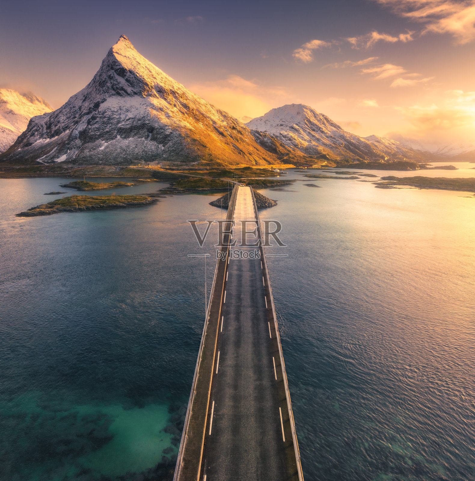 鸟瞰挪威罗弗敦群岛海上和雪山上的桥梁。冬日夕阳下的弗雷德旺桥。山水有碧水,岩石有雪,道路有云,天空有云。无人机俯视图照片摄影图片