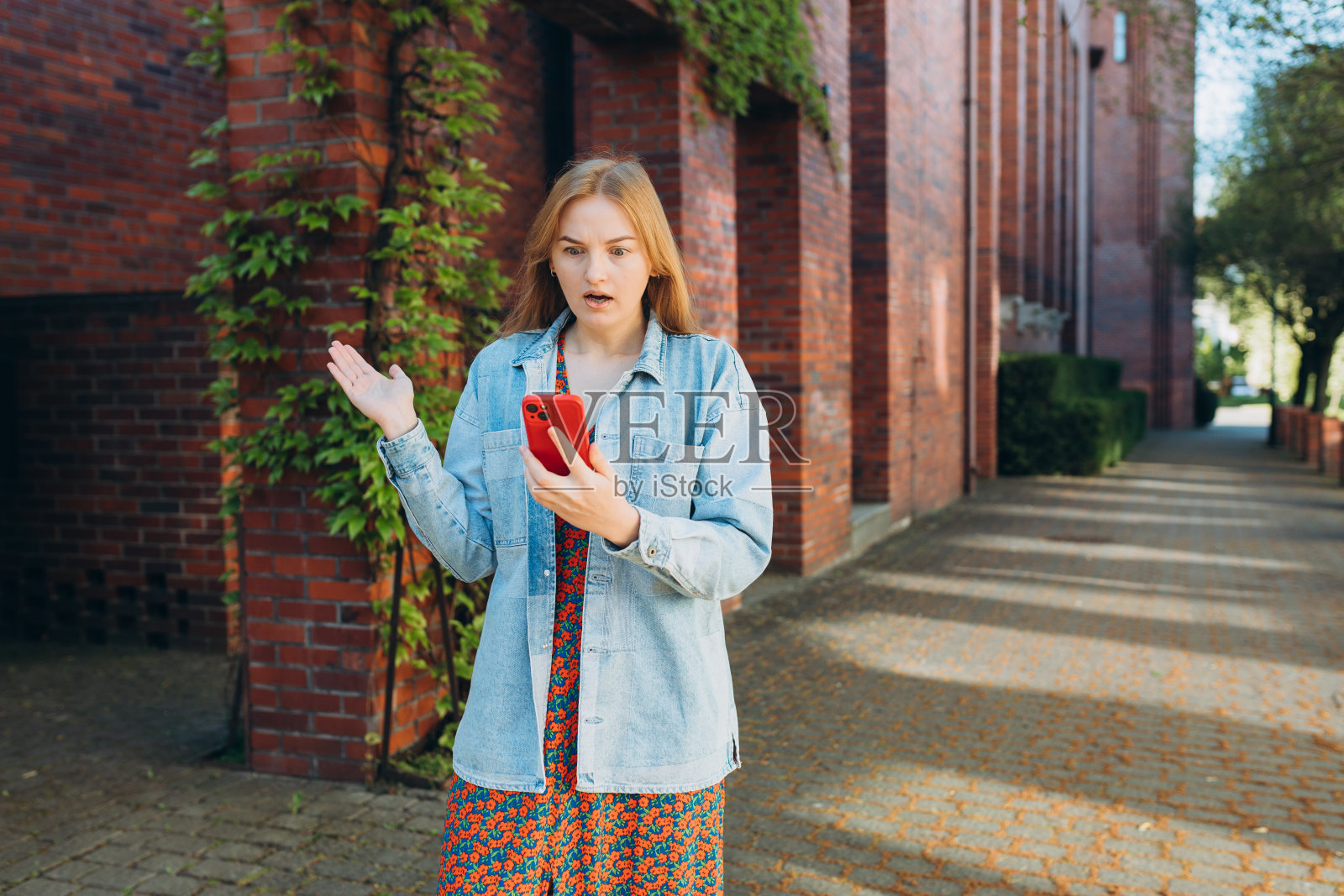 悲伤愤怒的女孩穿着衬衫,拿着手机站在城市街道上。消极的人的情绪。心烦意乱的30多岁年轻女性在户外使用智能手机…不好的感觉压力,焦虑,悲伤,情绪。照片摄影图片