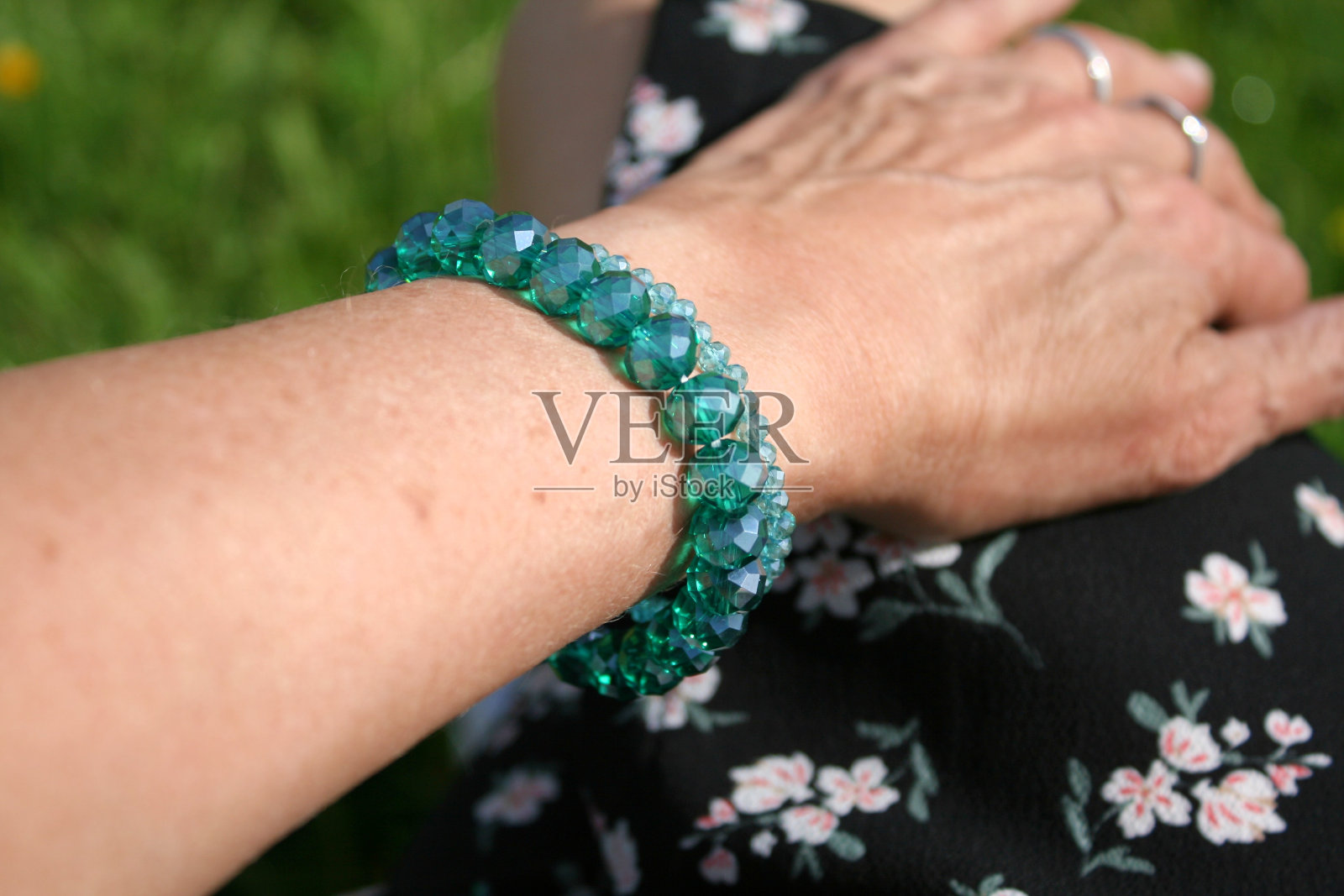 老妇人戴着绿松石手镯来搭配她的碎花连衣裙。照片摄影图片