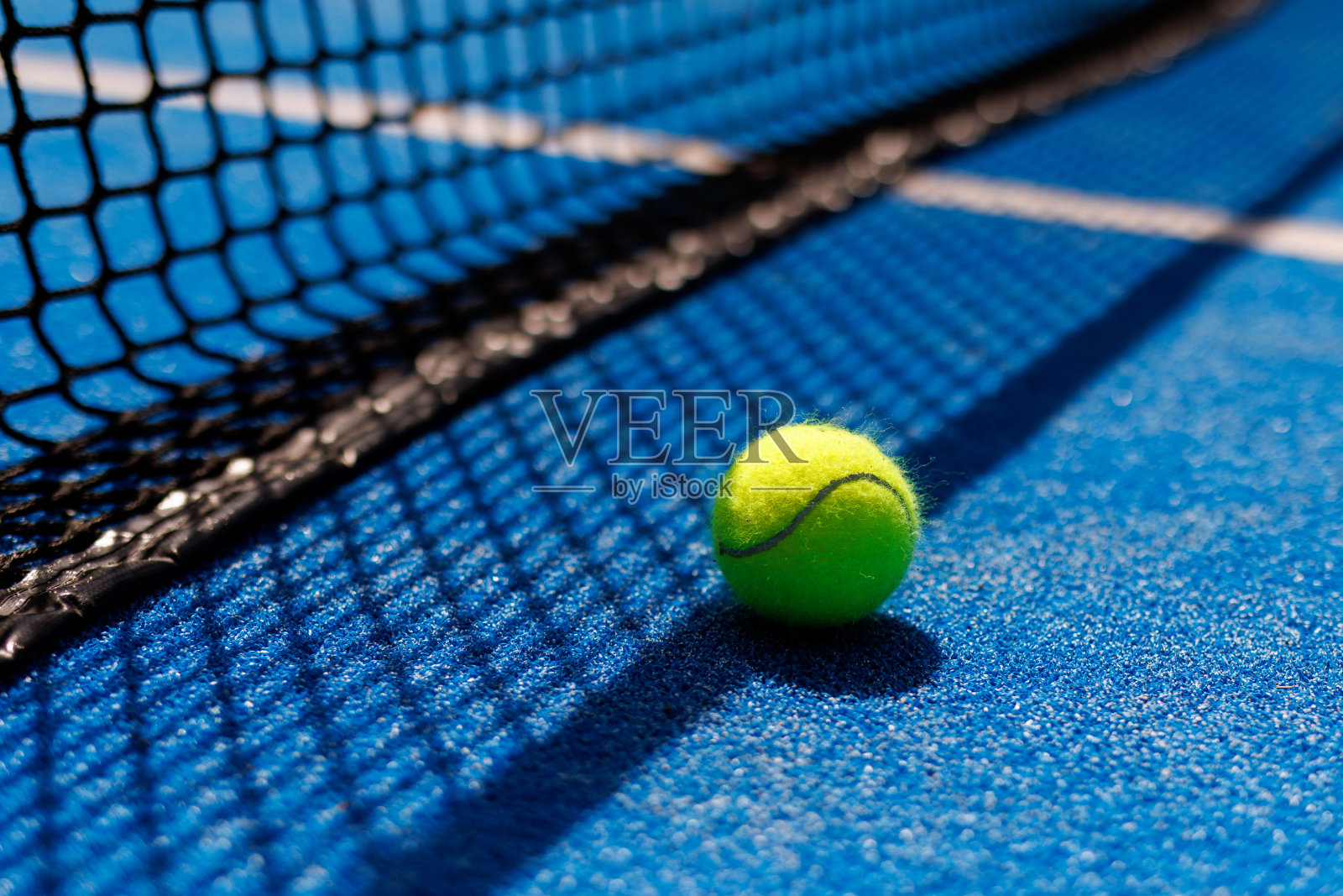 在一个蓝色的球拍网球场的网的阴影下的球照片摄影图片