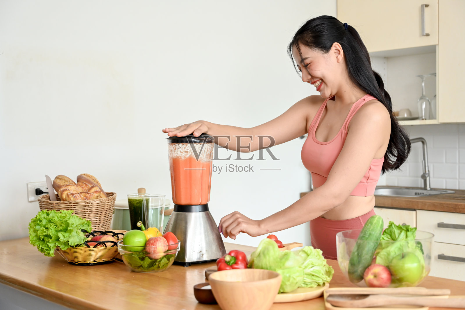 微笑的年轻女子在厨房用新鲜蔬菜制作冰沙。照片摄影图片
