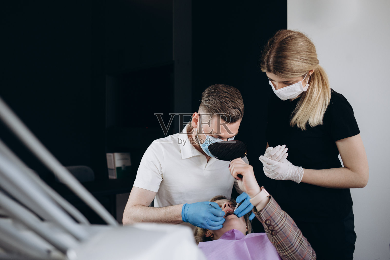 年轻有趣的正畸医生牙医白人男子穿着长袍,露出下颚咬牙的牙齿x光片病人妇女坐在牙医办公室的椅子室内橱柜附近的口腔医生。保健牙釉质治疗。照片摄影图片