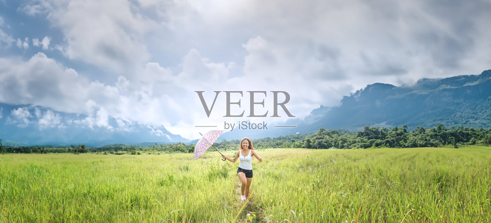 亚洲女性在假期旅行放松。在绿色的牧场上,伞的阳光在奔跑。照片摄影图片