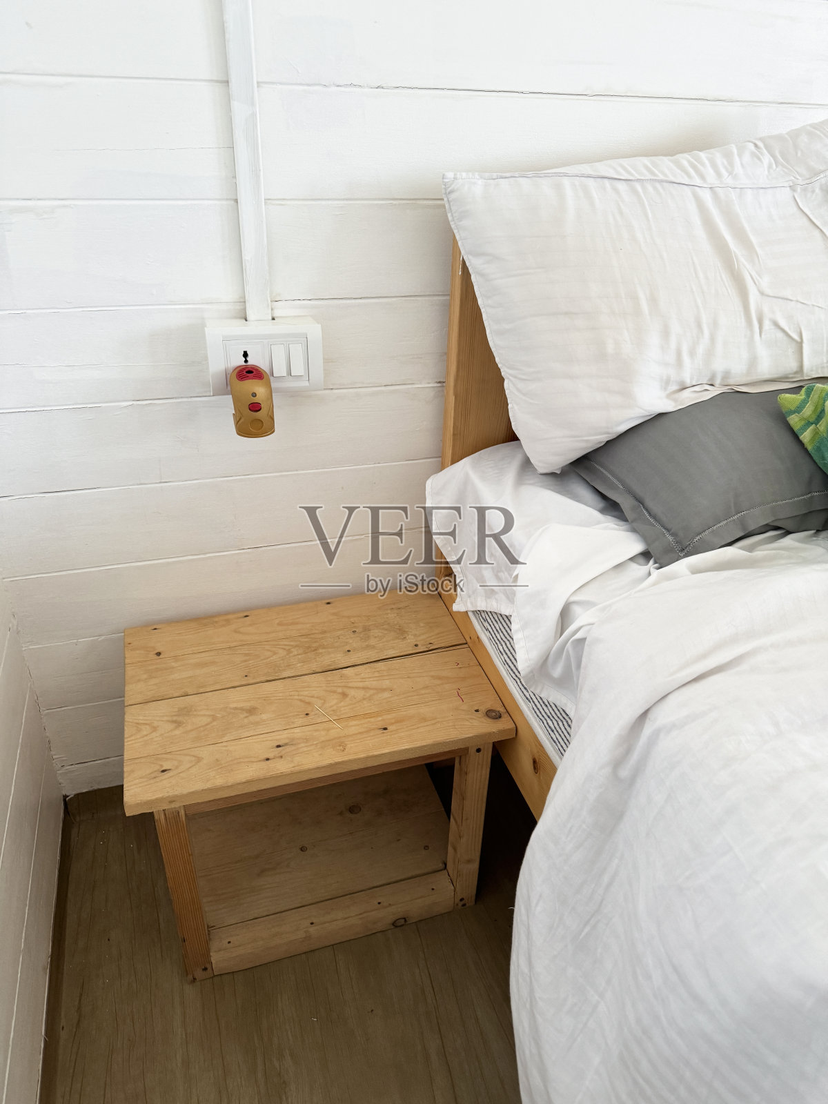 未整理的双人床,木制床头板,绿色条纹靠垫靠在白色和灰色的枕头上,凌乱的白色被套和床单,床头柜,插入驱蚊剂,重点放在前景上照片摄影图片