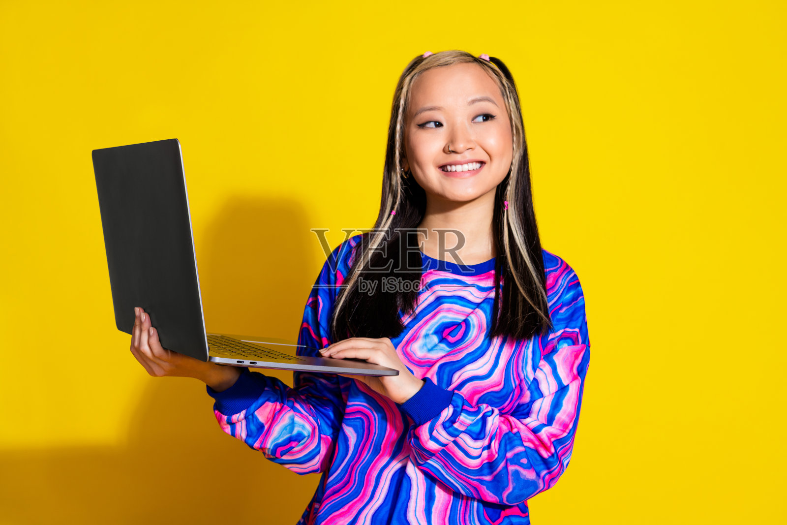 染了头发的聪明女人的肖像,穿着印花套头衫,拿着笔记本电脑,在黄色背景上提供孤立的空白空间照片摄影图片