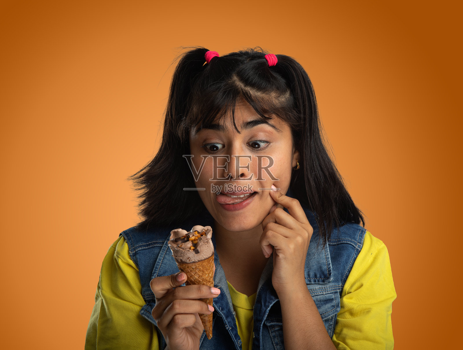 一个女人正在吃桔黄色背景的甜筒冰激凌照片摄影图片