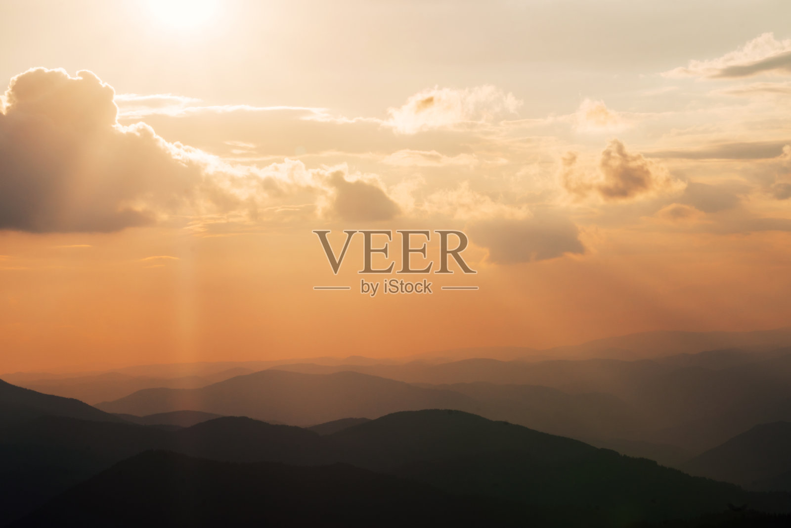 鸟瞰全景的山峰,美丽的山峰覆盖着树木在日落在夏天的晴天。夕阳西下,天空中泛着橘黄色的光芒。山脉的黑色剪影。太阳能反射照片摄影图片