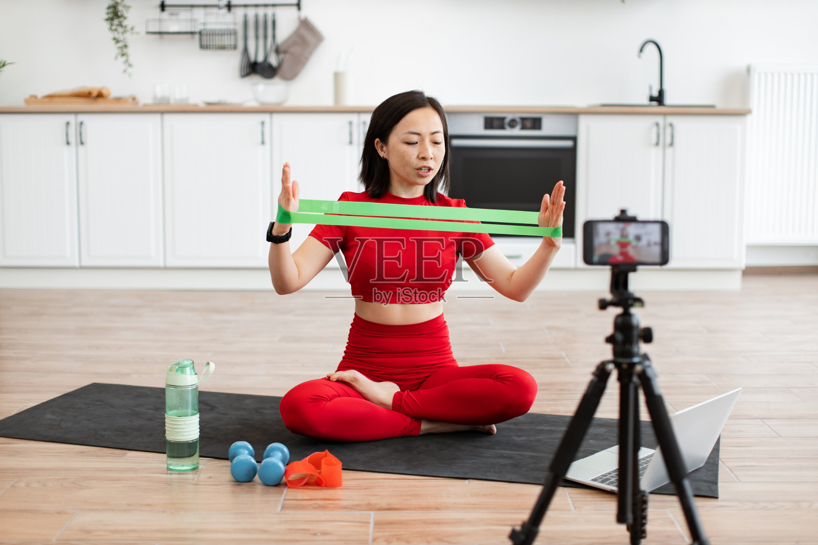 一名女子在厨房用阻力带教授在线健身课程照片摄影图片