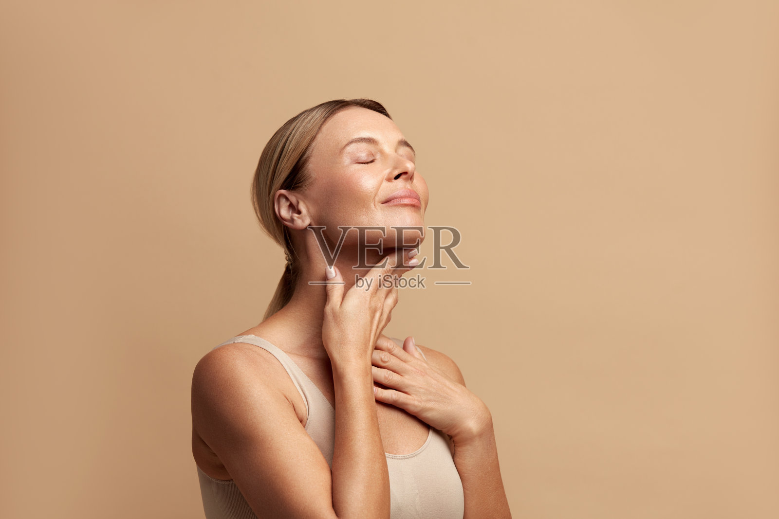 微笑的女人抚摸脖子。迷人的女人抚摸着她的皮肤,微笑着照片摄影图片