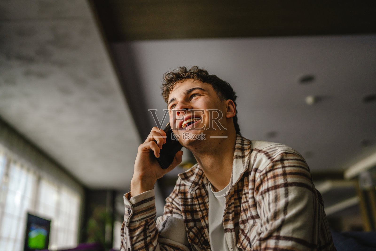 年轻的高加索男孩站在室内讲手机的肖像照片摄影图片