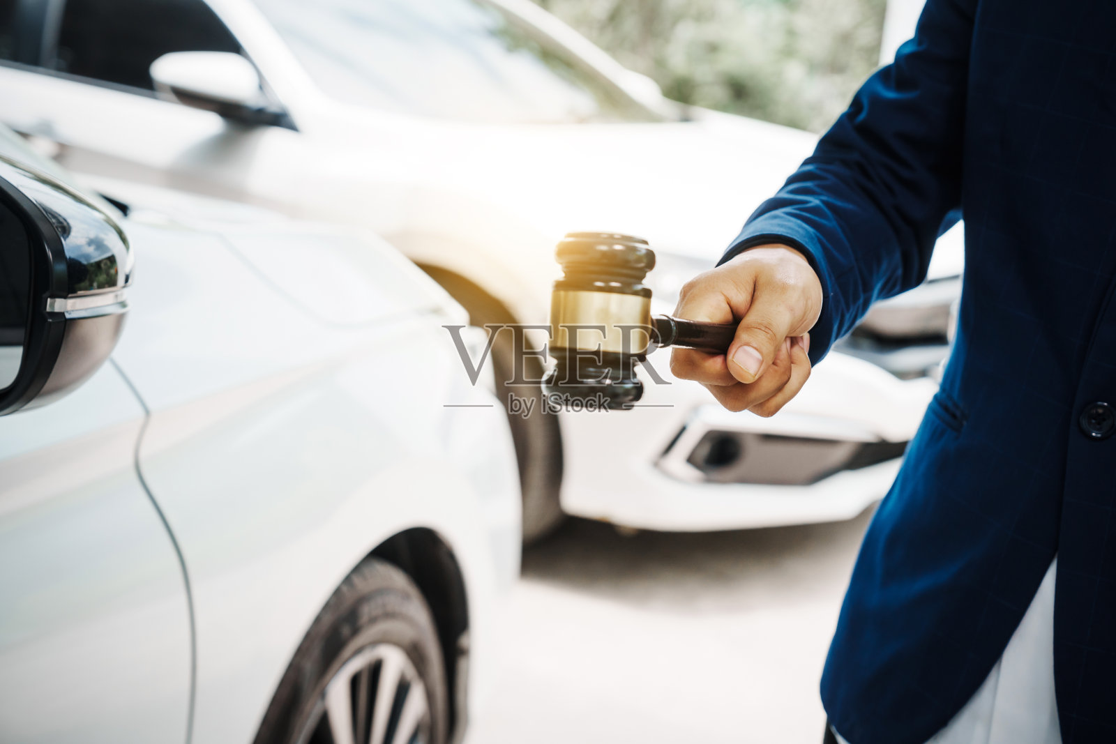 穿着西装的商人和拿着木槌的律师站在一辆汽车前,讨论着与交通违规有关的传票、责任和疏忽等法律问题。照片摄影图片