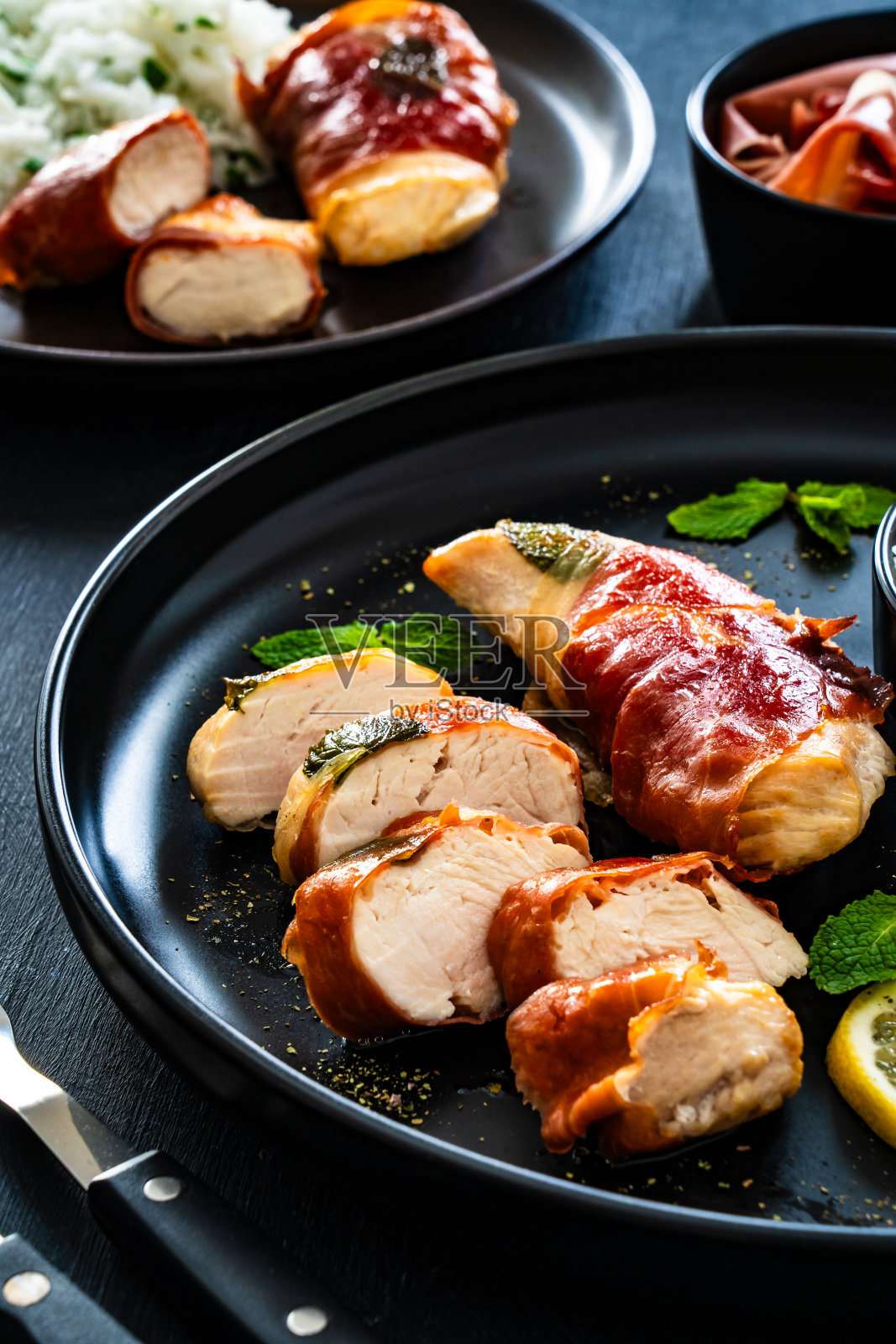 鸡肉Saltimbocca——黑色木桌上用意大利熏火腿片包裹的煎鸡肉片照片摄影图片