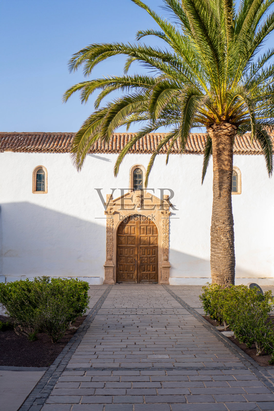 历史悠久的贝坦库利亚教堂入口,有棕榈树和蓝天照片摄影图片