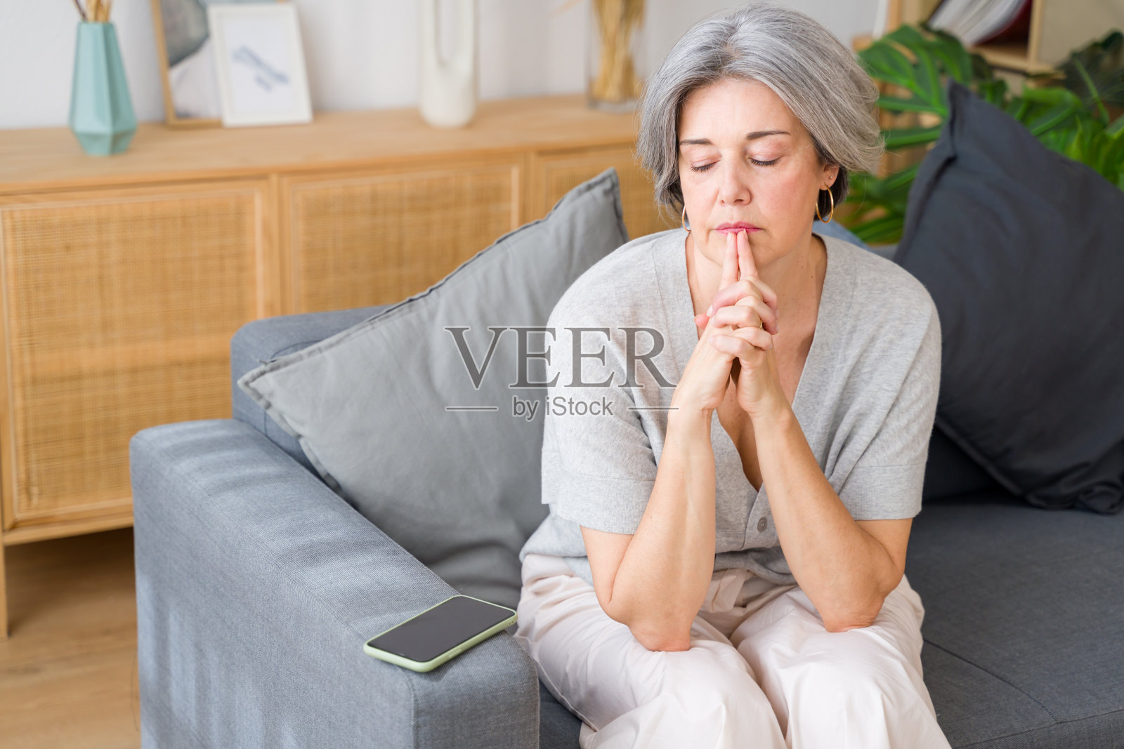 忧心忡忡的老妇人坐在家里的沙发上满怀希望地祈祷照片摄影图片