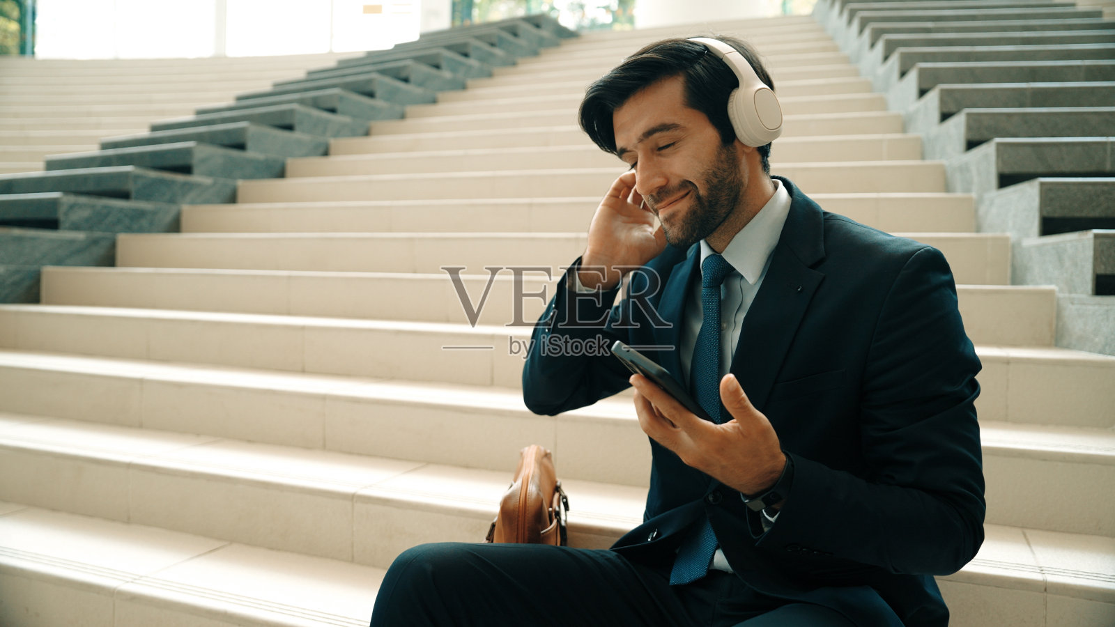 微笑的商人一边听音乐一边看手机。非常高兴的。照片摄影图片