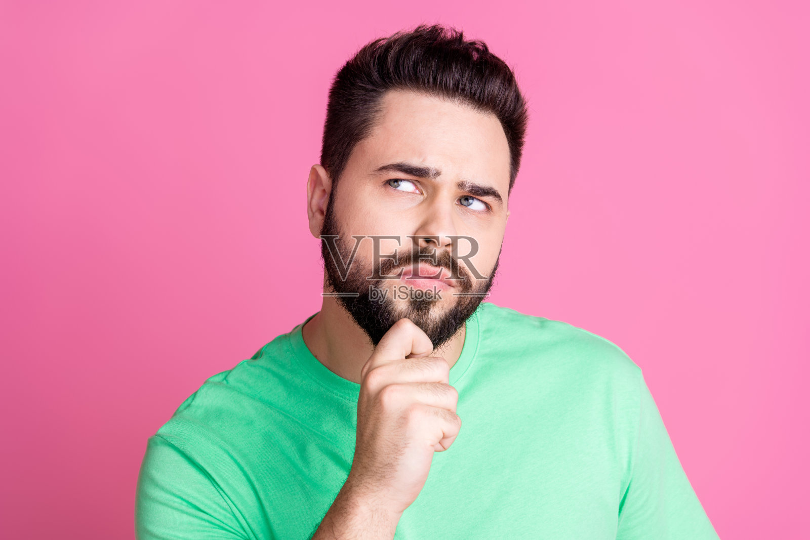 照片中,头脑聪明的家伙留着时髦的胡子,穿着绿色的t恤,在粉红色的背景上看宣传空白的空间照片摄影图片