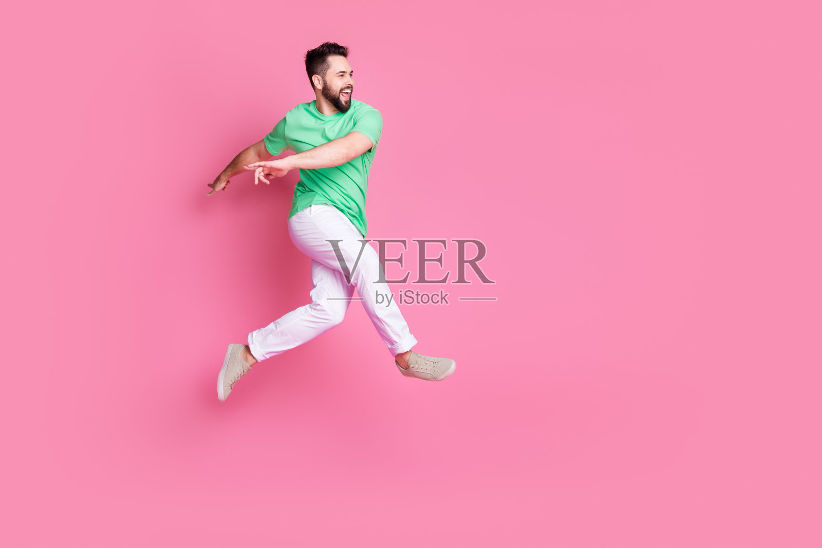 乐观的家伙穿着绿色t恤白色裤子跳跃的照片,在粉红色的背景上提供孤立的空白空间照片摄影图片