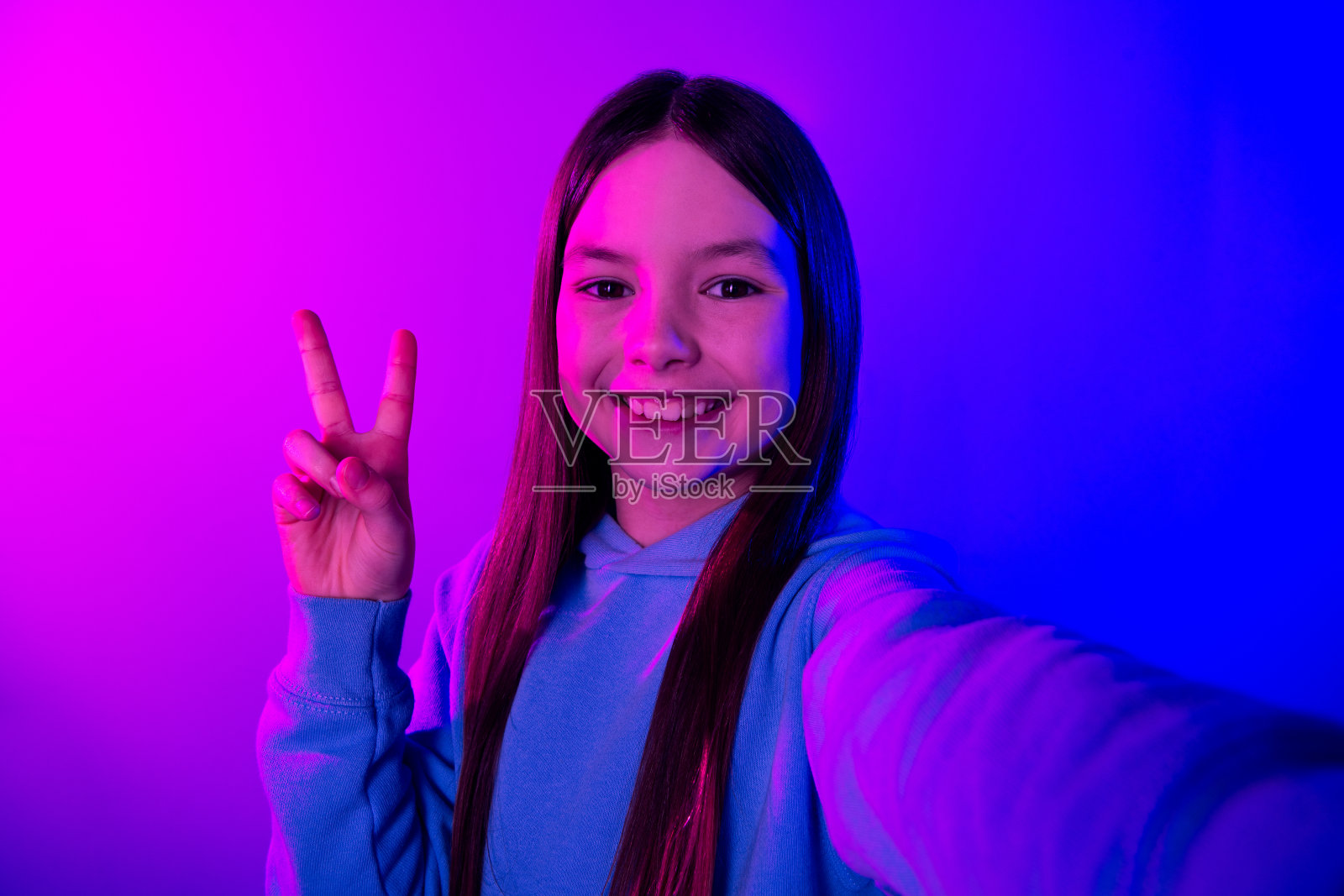 照片的开朗漂亮的小女士穿着连帽衫录制视频显示v标志孤立的霓虹紫色背景照片摄影图片