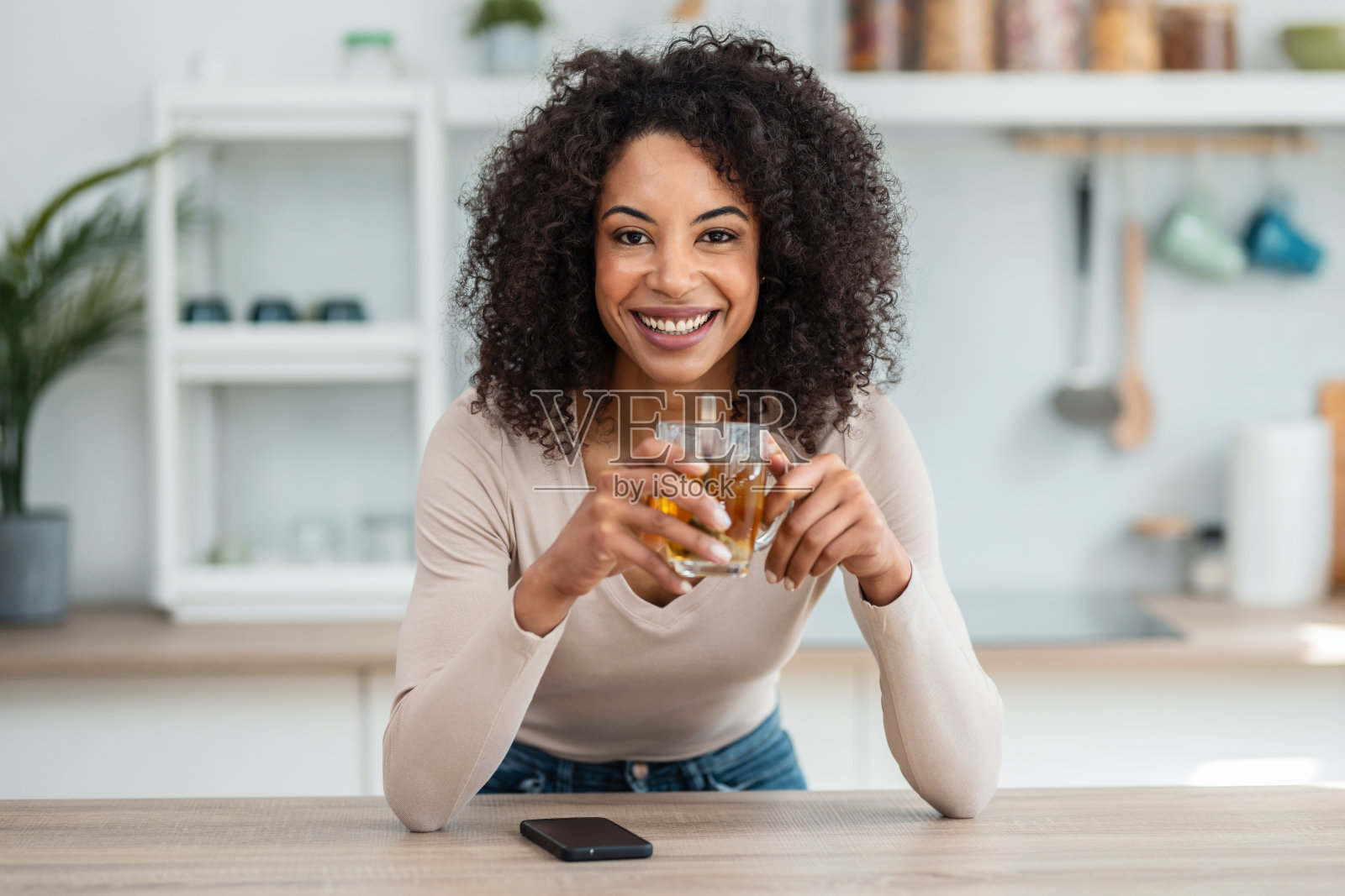 美女在家里的厨房边喝茶边看镜头。照片摄影图片