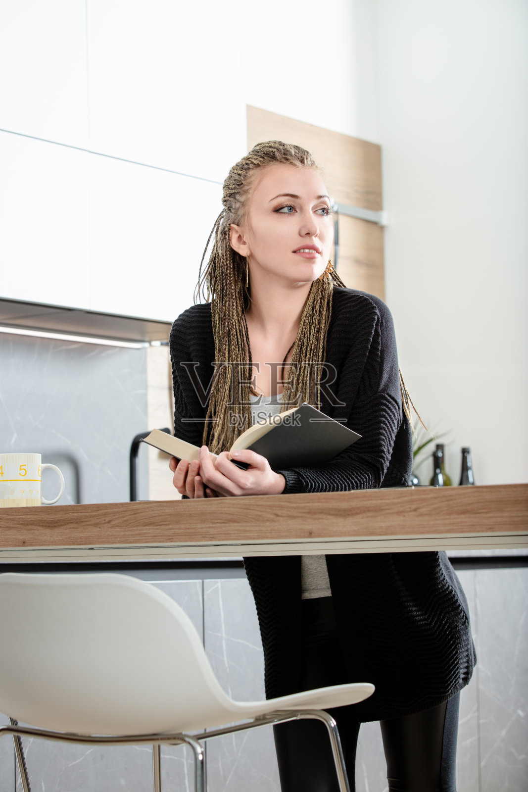 留着脏辫的年轻女子在现代厨房里看书照片摄影图片
