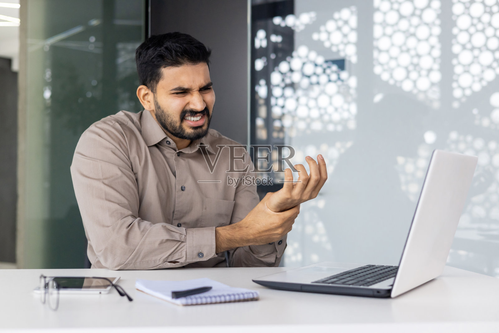 一位商人在一间以科技为中心的办公室里使用笔记本电脑时显得很不自在,这显示出重复性工作的紧张,并强调了这种环境中的压力和压力照片摄影图片