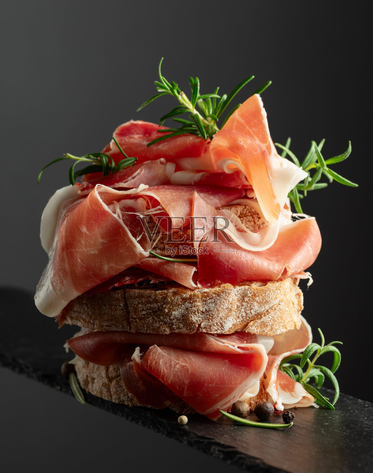 黑底熏火腿和迷迭香的意大利烤面包。照片摄影图片