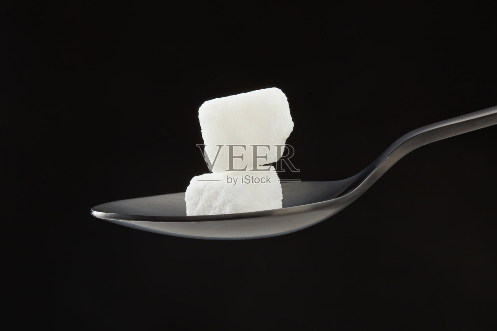 勺子里的方糖,背景是灰色的。照片摄影图片