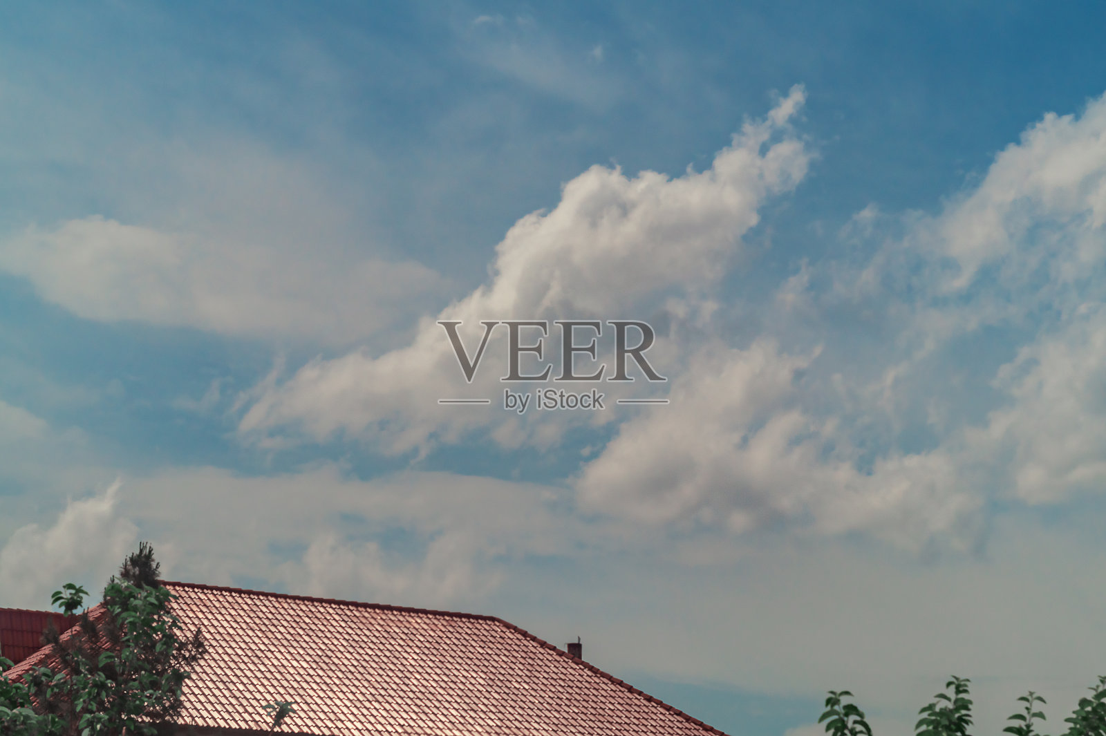 白云漂浮在天空中,在天空蓝色的背景下,有一种轻微模糊的阴霾。前景是房子的深红色屋顶。照片摄影图片