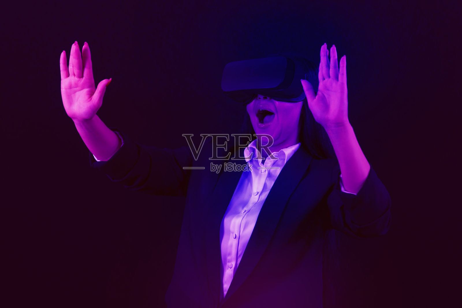 聪明的女性站在赛博朋克的霓虹灯下,戴着VR耳机,连接着虚拟世界,未来的网络空间社区技术。优雅女人用手触摸生成虚拟物体。幻觉。黑色背景。照片摄影图片