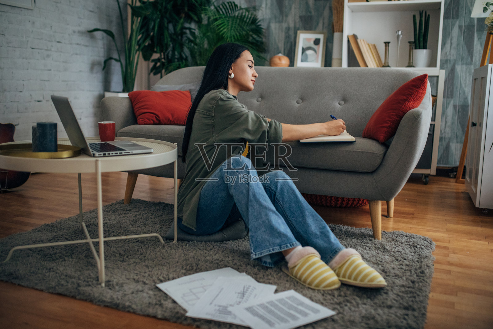 坐在沙发边写东西的人。照片摄影图片
